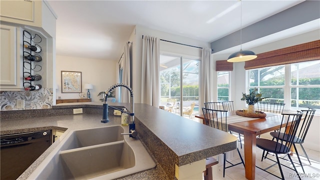 kitchen with pendant lighting, dark countertops, a sink, dishwasher, and a peninsula