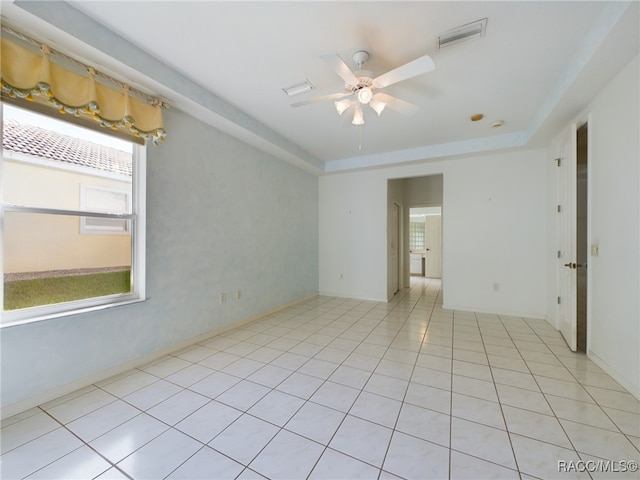 tiled empty room featuring a tray ceiling and ceiling fan