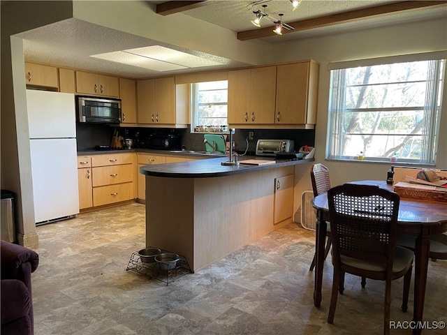 kitchen featuring dark countertops, freestanding refrigerator, a peninsula, light brown cabinetry, and black microwave