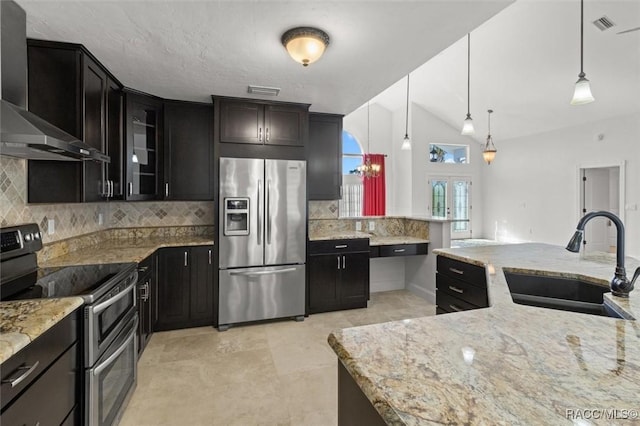 kitchen with tasteful backsplash, appliances with stainless steel finishes, a sink, light stone countertops, and wall chimney exhaust hood