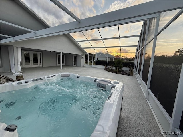 pool at dusk featuring glass enclosure, french doors, a patio area, and a hot tub