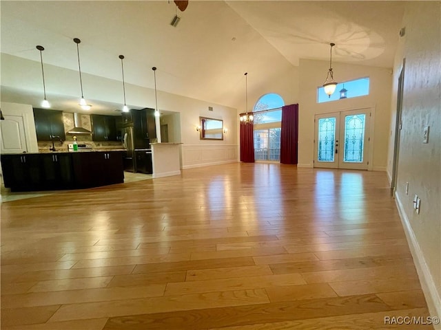 unfurnished living room with a chandelier, high vaulted ceiling, light wood-style flooring, visible vents, and french doors