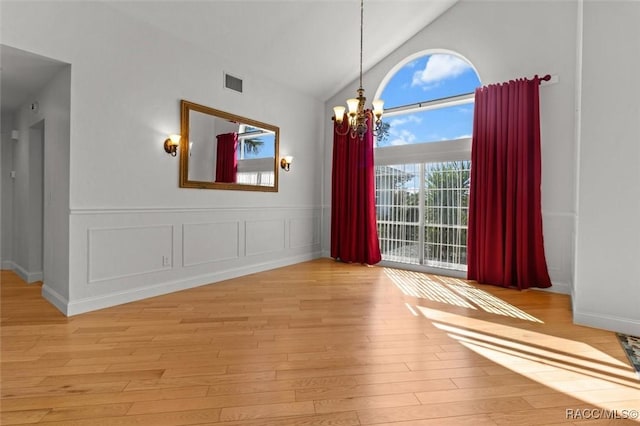 unfurnished dining area featuring visible vents, light wood-type flooring, high vaulted ceiling, a decorative wall, and a notable chandelier