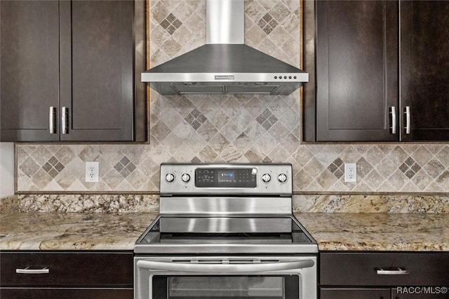 kitchen featuring light stone counters, dark brown cabinetry, wall chimney range hood, stainless steel electric range, and backsplash