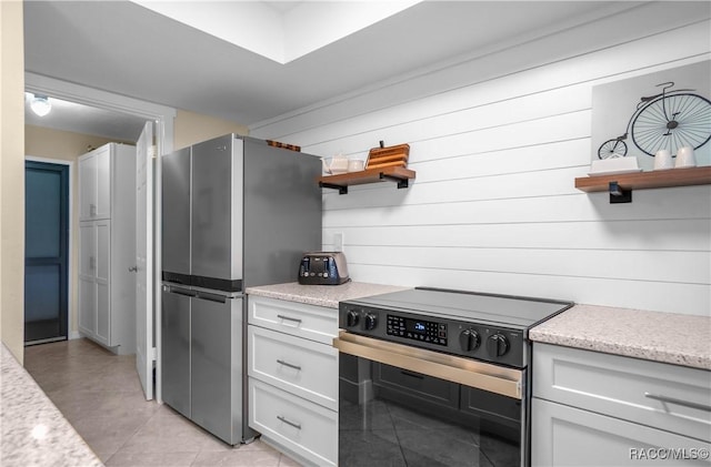 kitchen with white cabinetry, stainless steel fridge, black electric range, and wooden walls