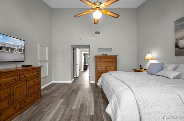 bedroom with ceiling fan, dark hardwood / wood-style floors, and a towering ceiling