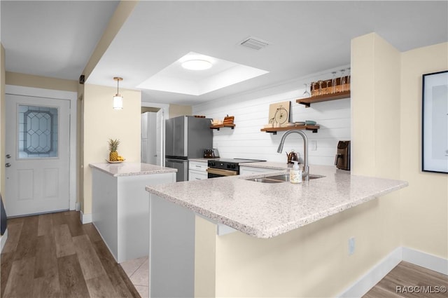 kitchen featuring pendant lighting, kitchen peninsula, sink, stainless steel refrigerator, and light wood-type flooring