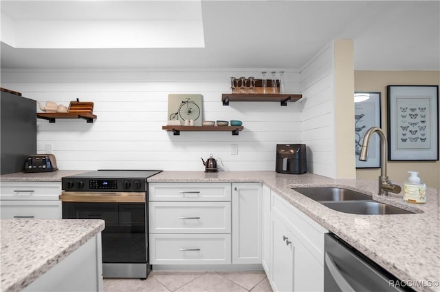 kitchen featuring black electric range, wood walls, sink, white cabinetry, and light stone counters