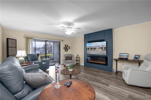 living room featuring ceiling fan, a large fireplace, and hardwood / wood-style floors