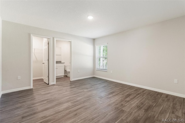 unfurnished bedroom featuring a walk in closet, connected bathroom, a closet, and dark wood-type flooring