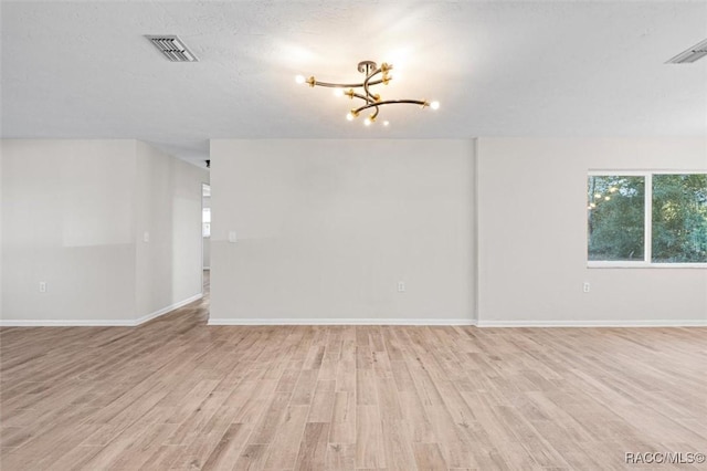 spare room with a textured ceiling, light wood-type flooring, and an inviting chandelier