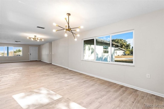 empty room with light hardwood / wood-style floors and an inviting chandelier