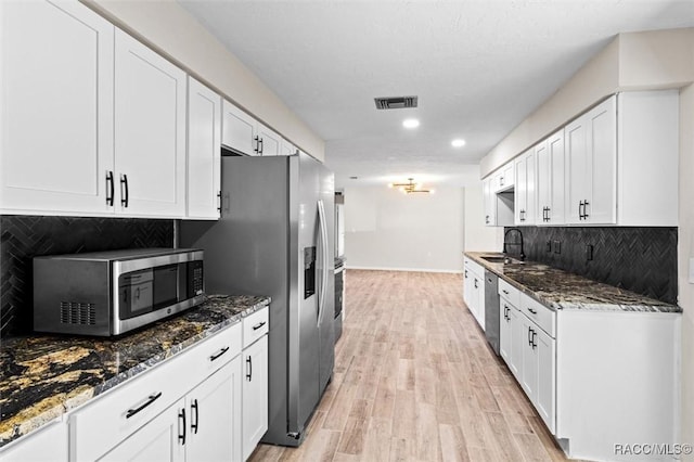 kitchen with dark stone countertops, white cabinetry, sink, and stainless steel appliances