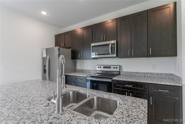 kitchen featuring dark brown cabinetry, stainless steel appliances, light stone countertops, and sink