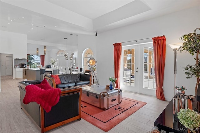 living room featuring light wood-type flooring, a tray ceiling, and french doors