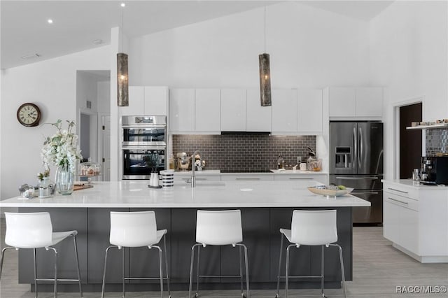 kitchen with a spacious island, appliances with stainless steel finishes, white cabinetry, decorative backsplash, and hanging light fixtures