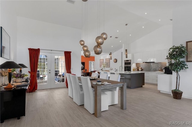 dining space with high vaulted ceiling, sink, light hardwood / wood-style flooring, and french doors