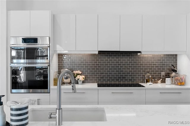 kitchen with stainless steel double oven, white cabinets, a sink, and modern cabinets