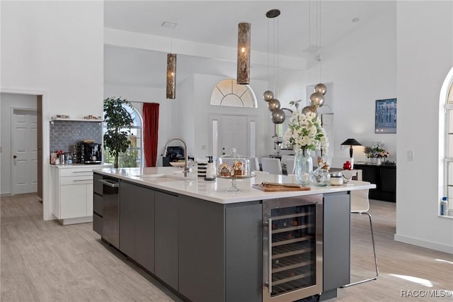 kitchen featuring a center island with sink, gray cabinetry, beverage cooler, pendant lighting, and white cabinets