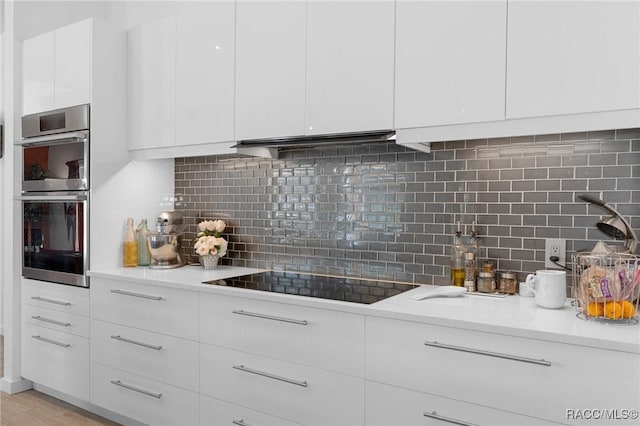 kitchen with double oven, black electric stovetop, white cabinets, and light countertops