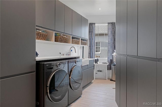 washroom featuring light wood-type flooring, cabinet space, a sink, and washing machine and clothes dryer