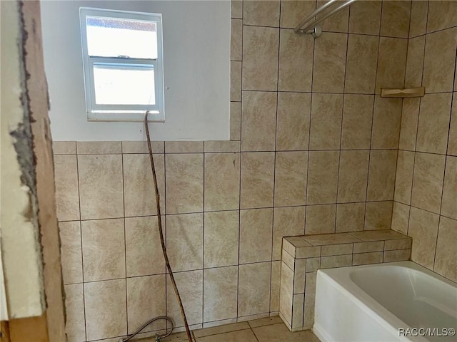 bathroom with tile patterned flooring, a bathtub, and tile walls