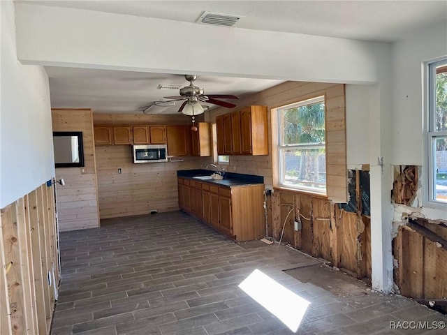 kitchen with sink, dark wood-type flooring, wooden walls, and ceiling fan