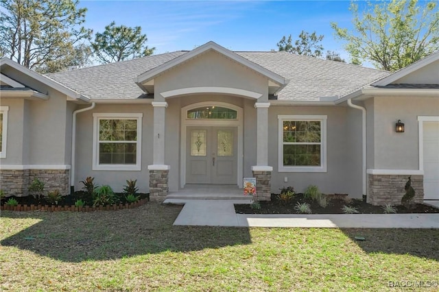 view of exterior entry with stucco siding, stone siding, a lawn, and a shingled roof