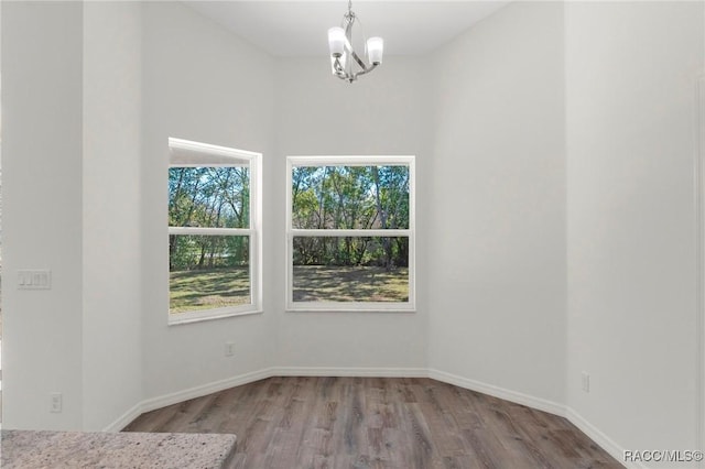 unfurnished dining area featuring a notable chandelier, plenty of natural light, baseboards, and wood finished floors