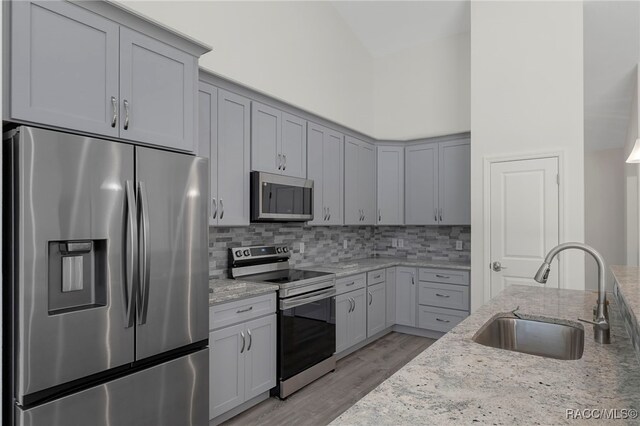 kitchen featuring light stone countertops, light wood-style flooring, a sink, and appliances with stainless steel finishes
