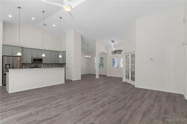 unfurnished living room featuring ceiling fan with notable chandelier, french doors, wood finished floors, arched walkways, and high vaulted ceiling