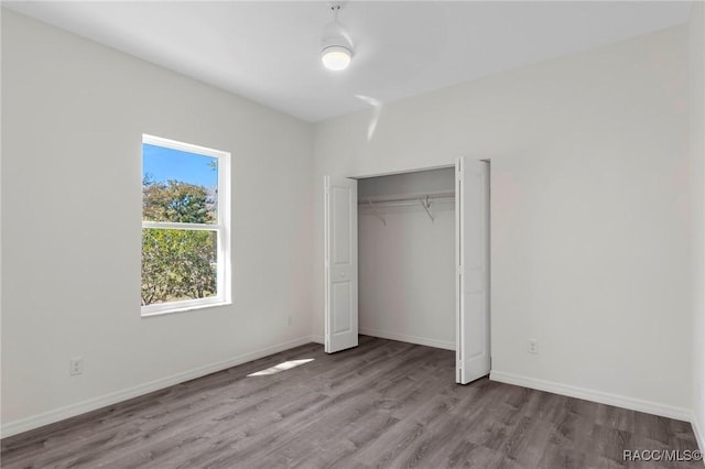 unfurnished bedroom featuring wood finished floors, baseboards, and a closet