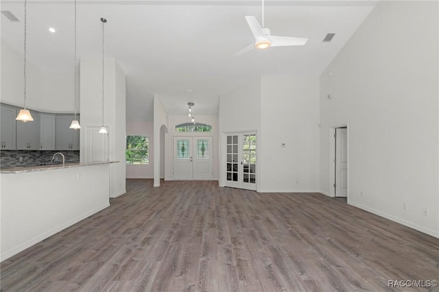 unfurnished living room with visible vents, wood finished floors, arched walkways, a high ceiling, and baseboards