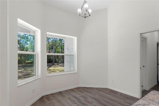 unfurnished dining area featuring a chandelier, baseboards, and wood finished floors