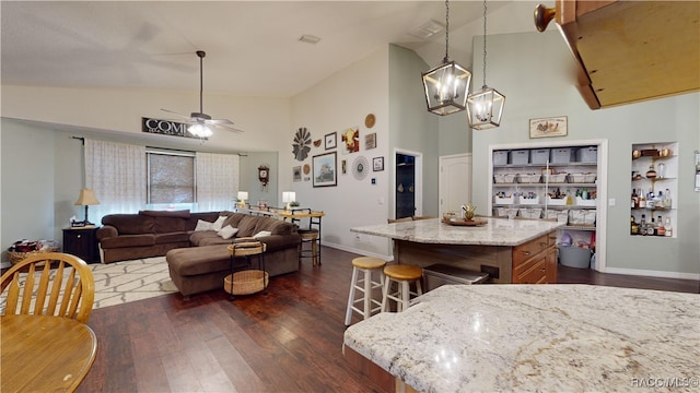 kitchen with a kitchen breakfast bar, ceiling fan with notable chandelier, a center island, dark hardwood / wood-style floors, and hanging light fixtures