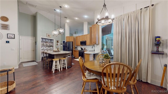 dining space featuring dark hardwood / wood-style flooring, high vaulted ceiling, an inviting chandelier, and sink