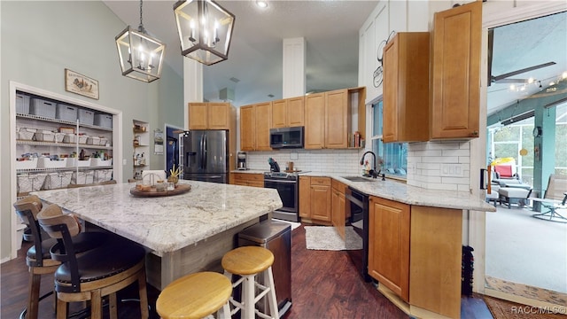 kitchen featuring dark wood-type flooring, hanging light fixtures, a towering ceiling, a kitchen island, and stainless steel appliances