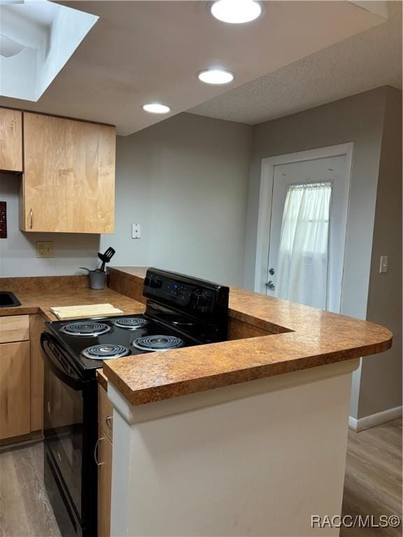 kitchen with black electric range oven, light brown cabinets, light wood-type flooring, and kitchen peninsula