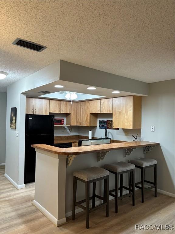 kitchen featuring black fridge, kitchen peninsula, light hardwood / wood-style floors, and a breakfast bar area