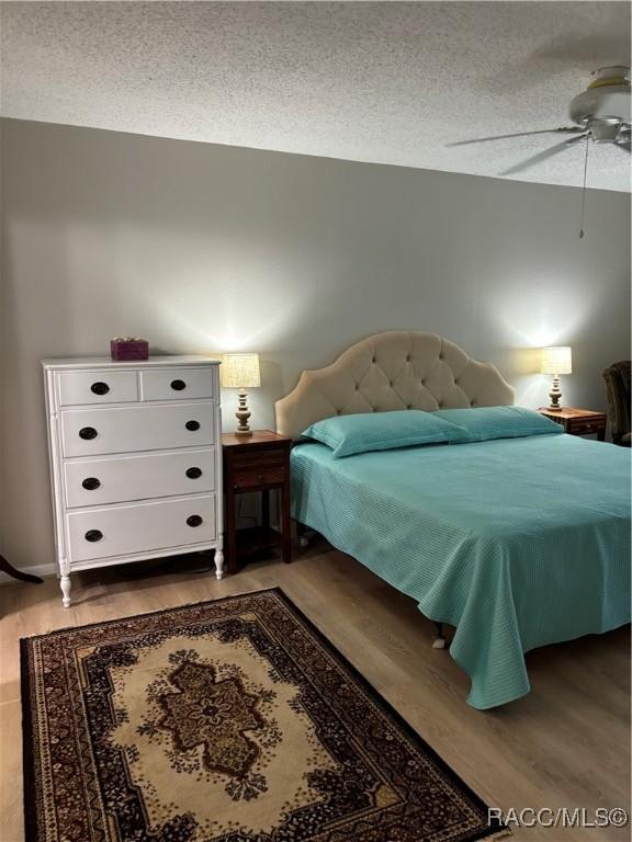 bedroom with wood-type flooring, ceiling fan, and a textured ceiling