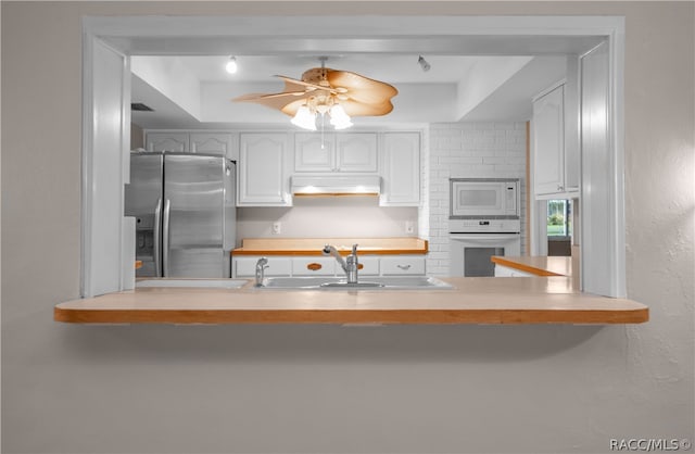 kitchen featuring white cabinets, a raised ceiling, white appliances, and sink