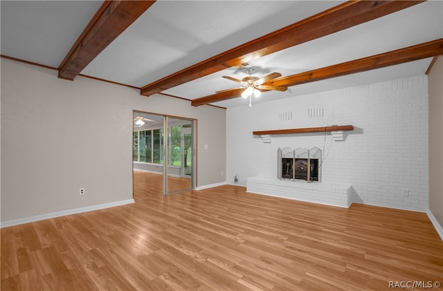 unfurnished living room featuring beam ceiling, ceiling fan, a brick fireplace, brick wall, and light wood-type flooring