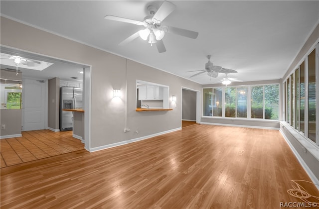 unfurnished living room featuring plenty of natural light, ceiling fan, sink, and light hardwood / wood-style flooring