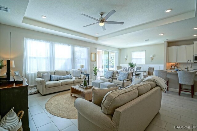 living room with a tray ceiling, light tile patterned flooring, visible vents, and ceiling fan