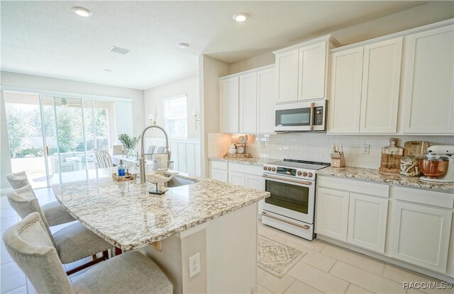 kitchen featuring a kitchen bar, white range with electric cooktop, a sink, light stone counters, and decorative backsplash