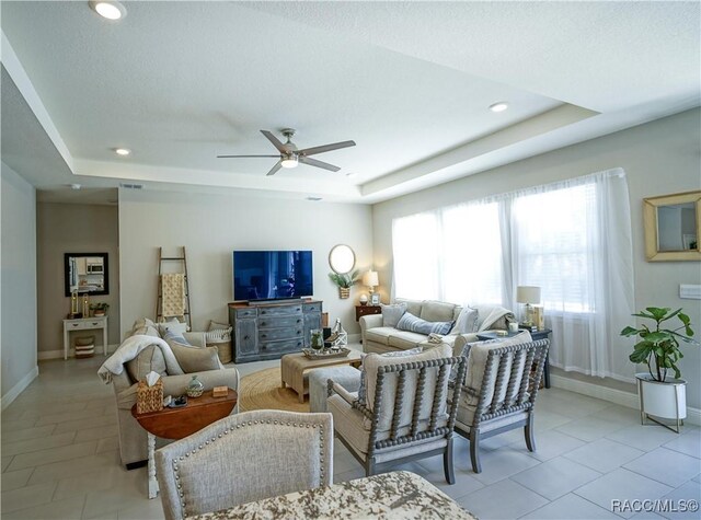 living area with light tile patterned floors, a tray ceiling, and baseboards