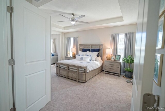 carpeted bedroom featuring a raised ceiling and ceiling fan