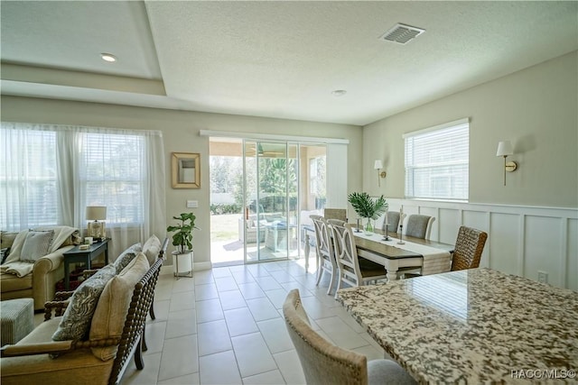 dining space featuring visible vents, plenty of natural light, a textured ceiling, and a decorative wall