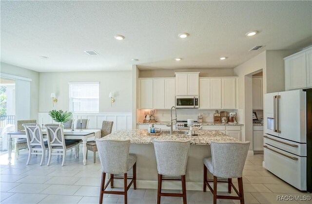 kitchen featuring stainless steel microwave, visible vents, high end white fridge, light stone counters, and a sink