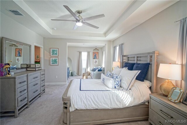 bedroom featuring a ceiling fan, visible vents, baseboards, a tray ceiling, and light colored carpet